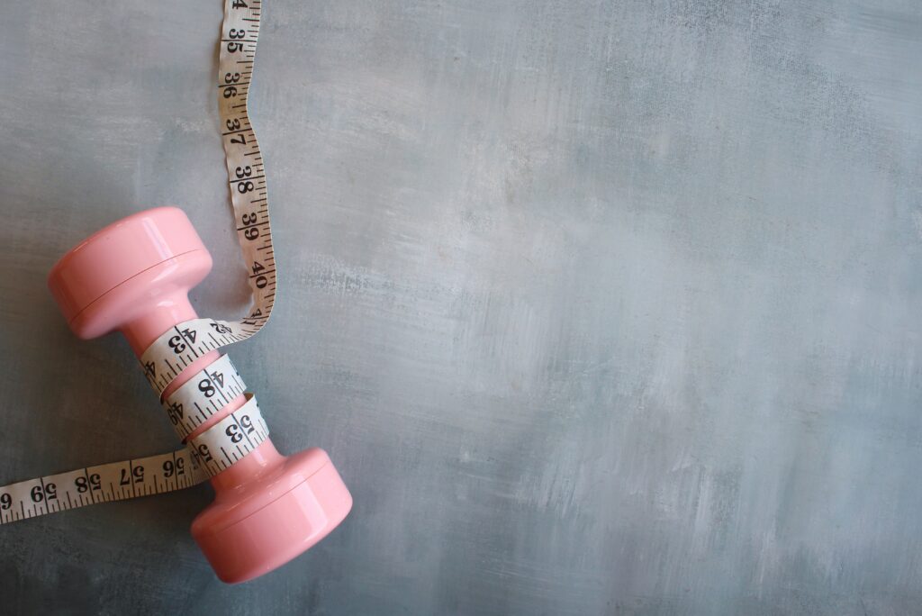 fitness weight management concept pink dumbbell measuring tape concrete floor